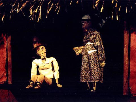 Bonecos de papel machê, um homem sentado e uma mulher em pé com uma cesta nos braços, são os pais de Nanã.